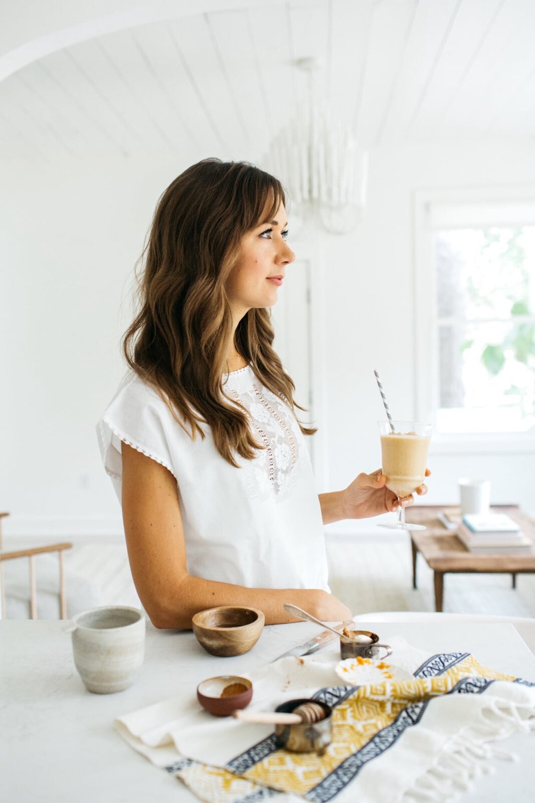 A woman holding a pumpkin spice smoothie at a bright breakfast table