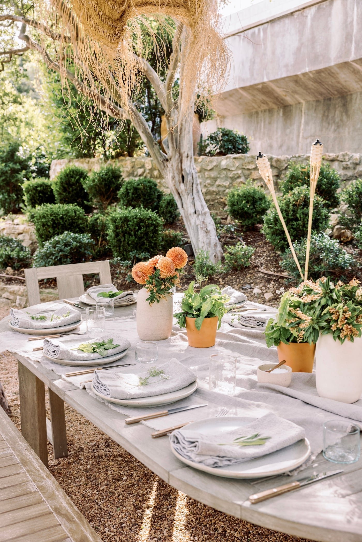 A long backyard table set with white linens, plates, and flowers