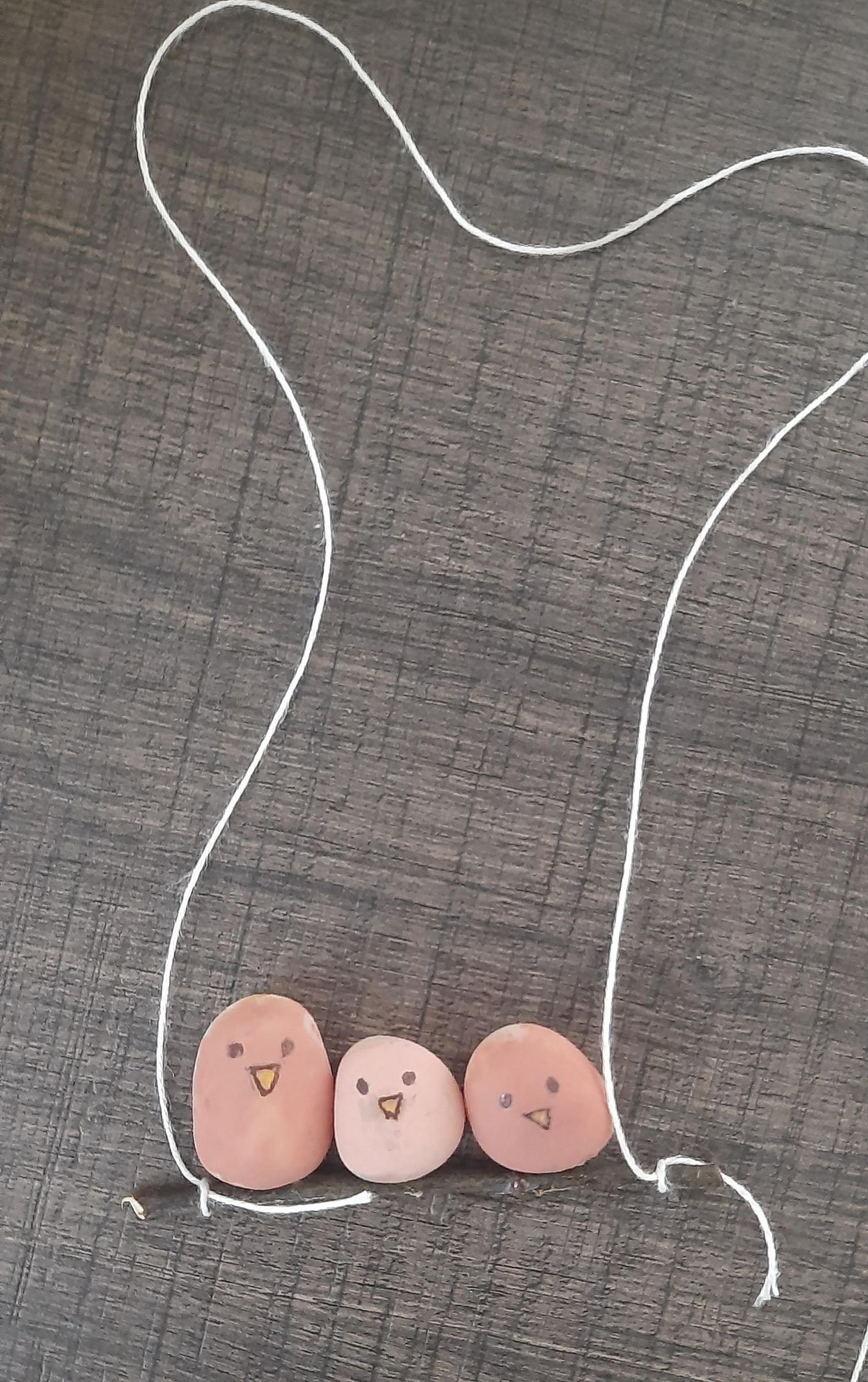 A completed pebble sparrow branch hanging from cord tied at both ends