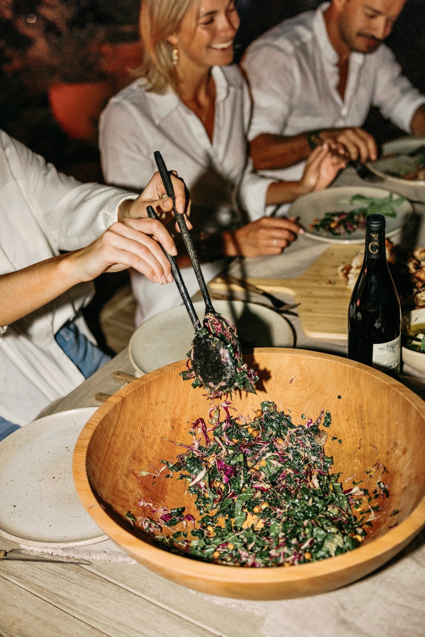 Guests serving a colorful salad at a candlelit dinner